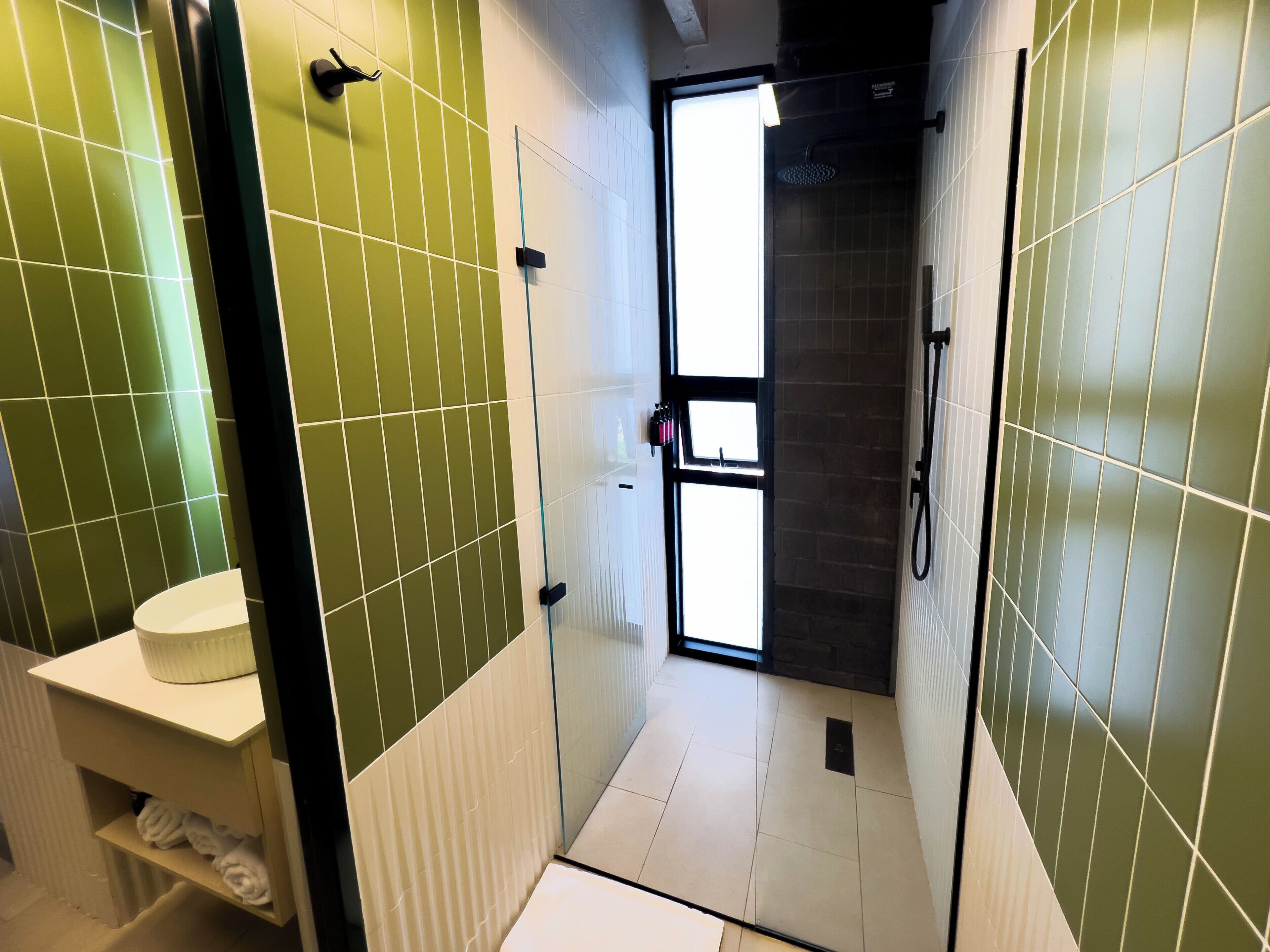 A bathroom with green tiled walls, a white sink, and a glass shower enclosure.