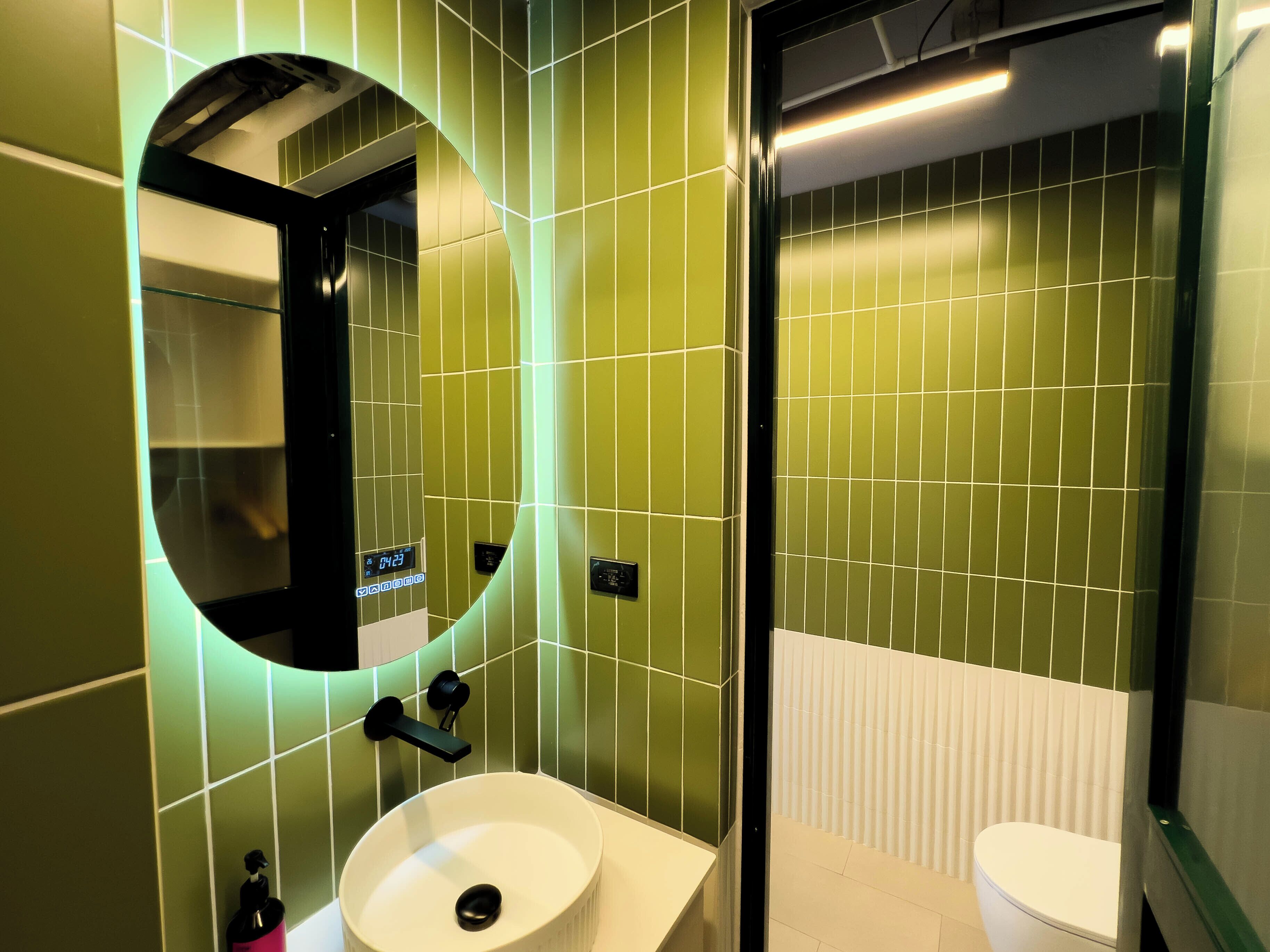 A bathroom with green tiled walls, a white sink, and a toilet.