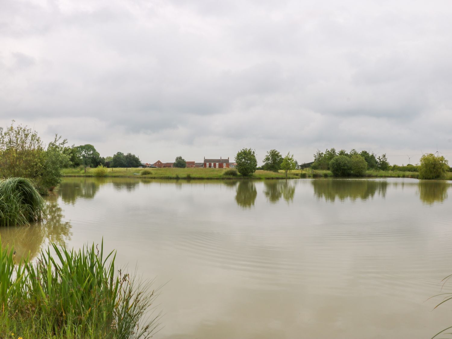 Un lago tranquillo con un edificio rosso all'orizzonte, immerso nel verde.