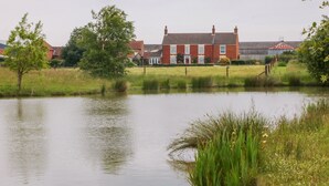 A large red brick house with a white door and windows, surrounded by a grassy field and a pond. - Barn Owl (Louth)