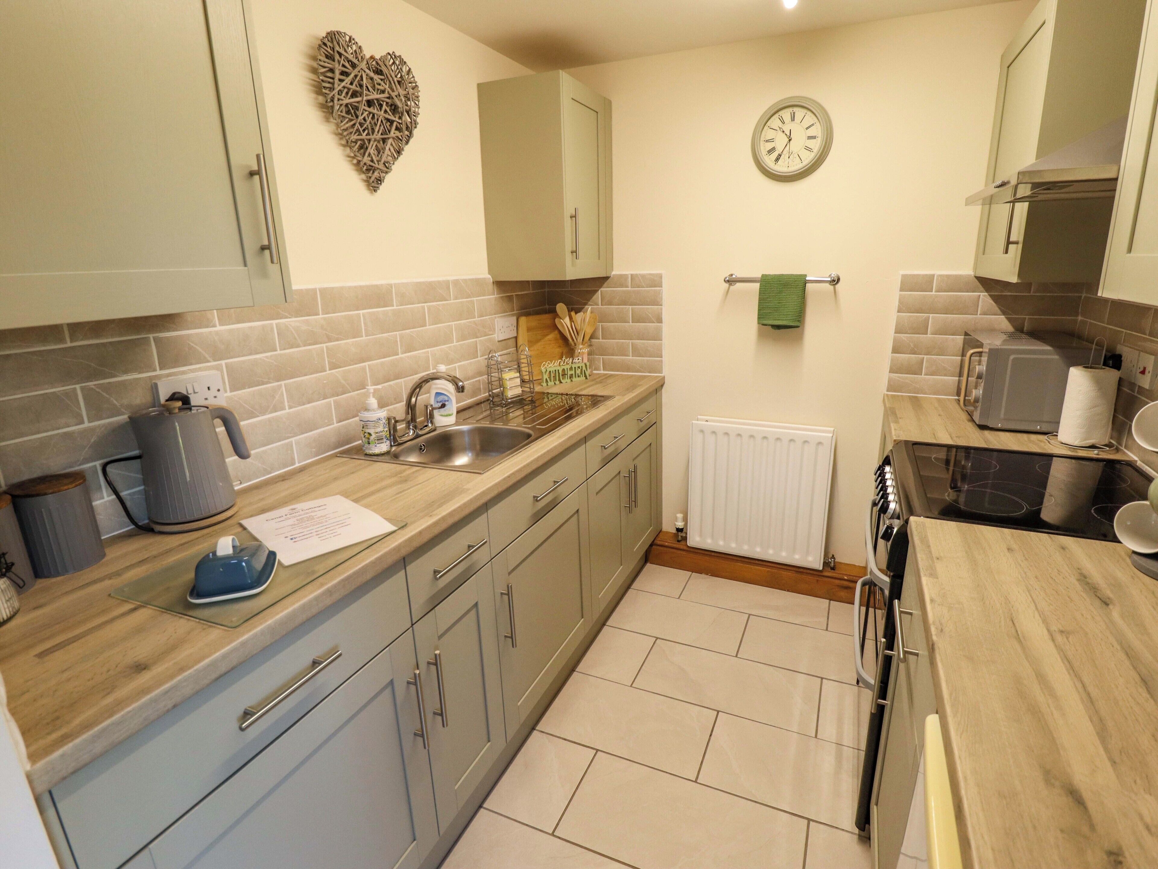A kitchen with grey cabinets, a sink, a kettle, a toaster, and a clock on the wall.
