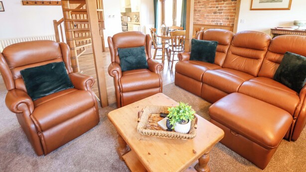 A living room with leather sofas, a wooden coffee table, and a spiral staircase. - Barn Owl (Louth)