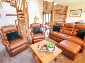 A living room with leather sofas, a wooden coffee table, and a spiral staircase. - Barn Owl (Louth)