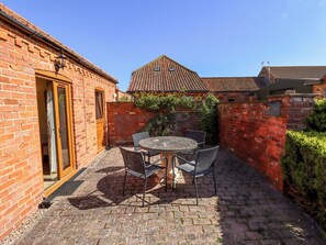 A brick building with a tiled roof, a patio with a round table and chairs, and a door leading to an interior space. - Kingfisher (Louth)
