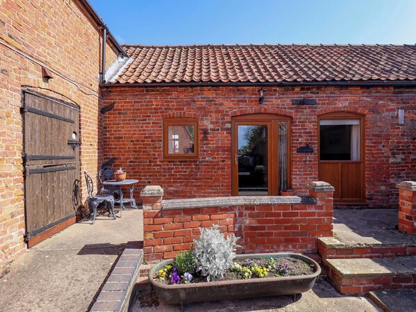 A brick building with a tiled roof, a wooden door, and a small garden with flowers. - Ticklepenny (Louth)