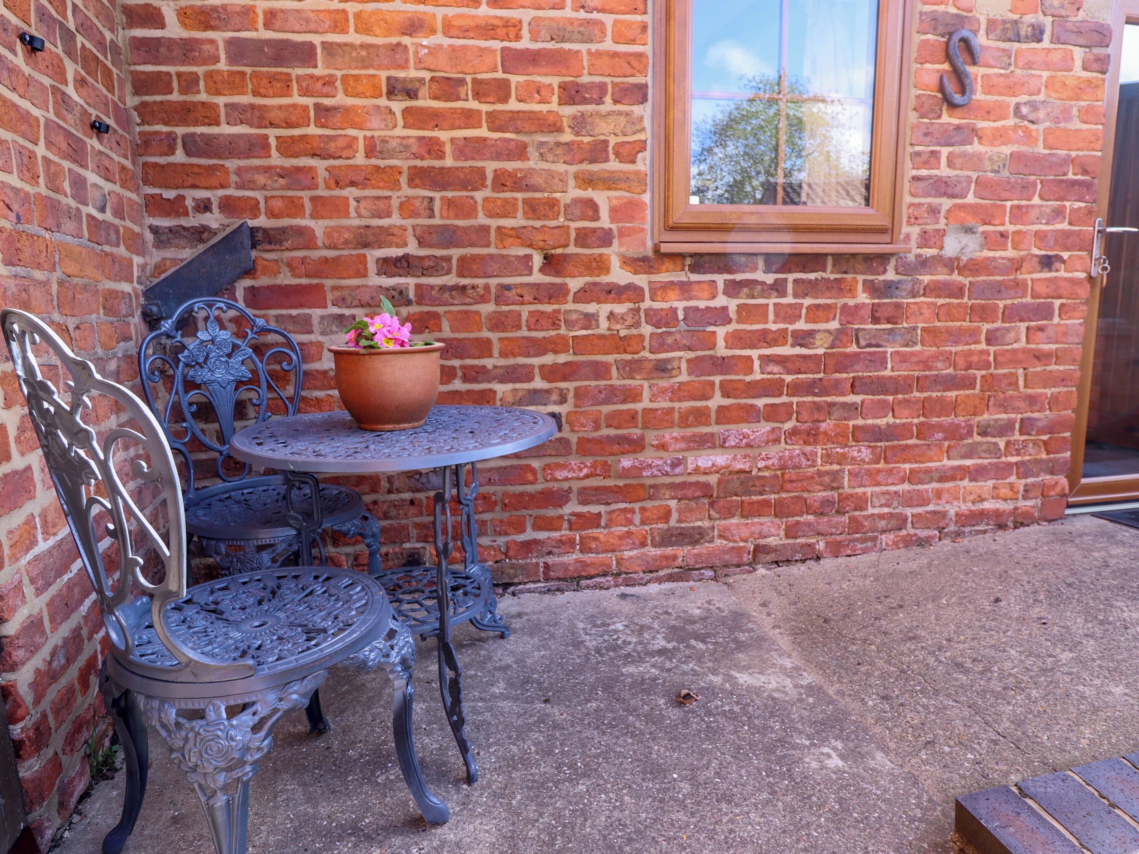A brick wall with a window, a metal table with chairs, and a potted plant.
