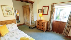 A bedroom with a bed, a wooden dresser, a chair, a lamp, and a window with curtains. - Ticklepenny (Louth)