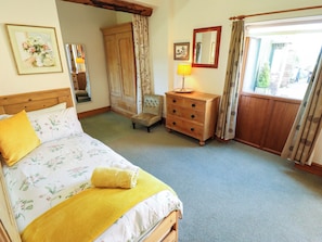 A bedroom with a bed, a wooden dresser, a chair, a lamp, and a window with curtains. - Ticklepenny (Louth)
