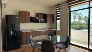 A modern kitchen with a black refrigerator, wooden cabinets, a granite countertop, and a glass dining table with four chairs. - Depa A few blocks from the Beach and Golden Zone ByGPS (Mazatlán)