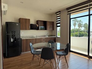 Eine moderne Küche mit einem schwarzen Kühlschrank, Holzschränken, einer Granit-Arbeitsplatte und einem Glastisch mit vier Stühlen.