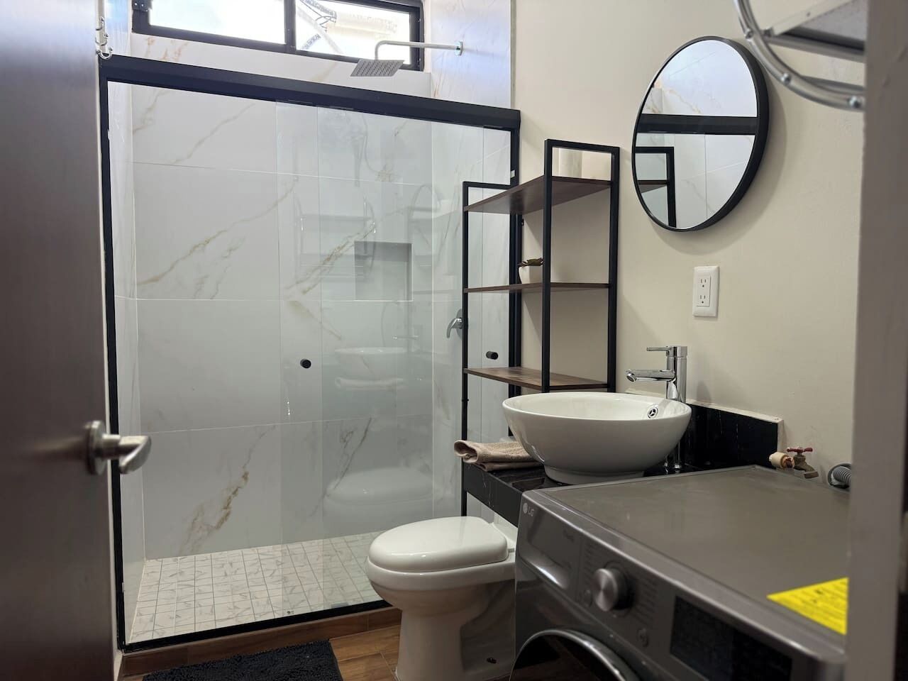 A bathroom with a glass shower enclosure, a toilet, a sink, and a mirror.