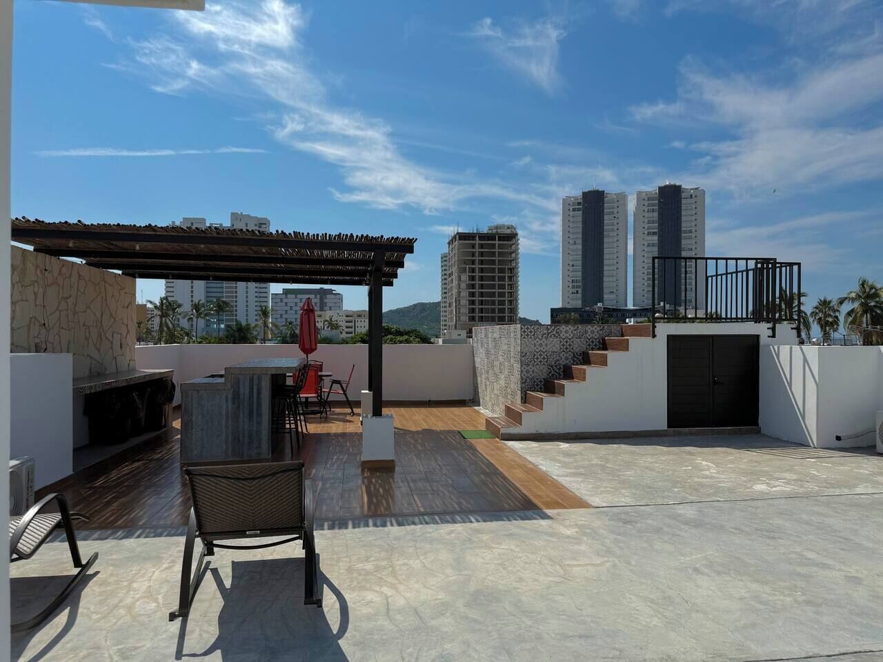 A rooftop terrace with a pergola, seating area, and a view of tall buildings.
