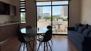 A modern living room with a glass dining table, dark sofas, and a large window offering a city view. - Depa A few blocks from the Beach and Golden Zone ByGPS (Mazatlán)