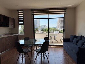 Ein modernes Wohnzimmer mit einem Glastisch, dunklen Sofas und einem großen Fenster mit Blick auf die Stadt.