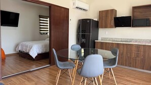 A compact living space with a bed, a glass dining table with chairs, a kitchen area with a refrigerator and microwave, and a TV mounted on the wall. - Depa A few blocks from the Beach and Golden Zone ByGPS (Mazatlán)