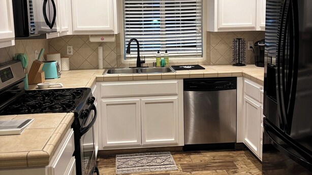 A modern kitchen with white cabinets, stainless steel appliances, a black refrigerator, and a window with blinds. - Spacious 4-bedroom house, perfect for entertaining in the heart of Ridgecrest. (Ridgecrest)