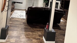 A spacious living area with a dark leather sofa, wooden flooring, and a ceiling fan. An archway leads to a room with a sign reading "LOVE GATHERS HERE." - Spacious 4-bedroom house, perfect for entertaining in the heart of Ridgecrest. (Ridgecrest)