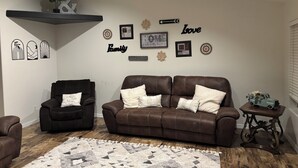 A living room with a brown leather sofa, a black armchair, and a patterned rug. - Spacious 4-bedroom house, perfect for entertaining in the heart of Ridgecrest. (Ridgecrest)