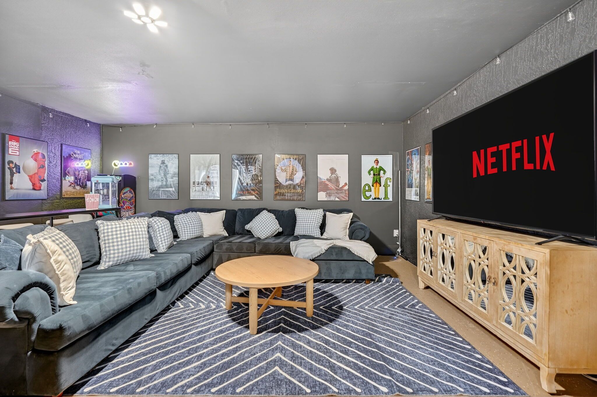 Un salon moderne avec un canapé d’angle, une table basse ronde et un grand téléviseur à écran plat affichant le logo de Netflix.