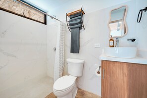 Een badkamer met een wit toilet, een houten kastje, een marmeren wand, een handdoekhouder en een douchegordijn.
