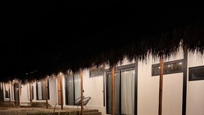 En rad vita byggnader med halmtak, numrerade dörrar och en grusbelagd mark.