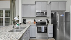 Cozinha com bancadas de granito, eletrodomésticos de aço inoxidável e armários em cinza claro.