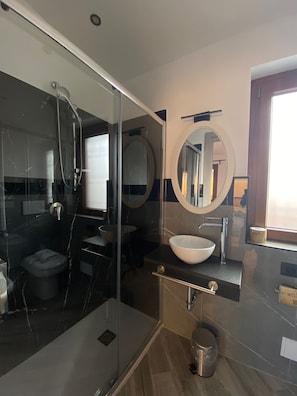 A modern bathroom with a glass shower enclosure, a round mirror, a white sink, and a toilet. - Il Piccolo Borghetto (Rome)