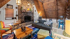 A cozy loft-style room with a stone fireplace, wooden beams, and a colorful rug. - A-Frame w/ VIEWS | Walk to Downtown/Park | Pets OK (Mentone)