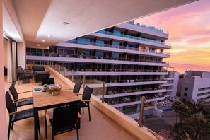 A multi-story hotel with outdoor seating on the balcony, offering views of the city skyline and sunset. - Steps to Medano Beach | 3BR Condo Sleeps 8 (El Medano Beach)