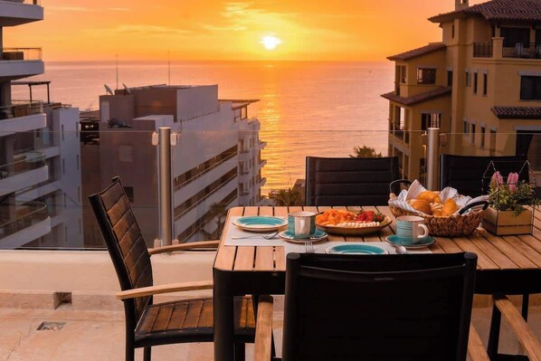 A table set for breakfast with a view of the sunset over the sea, overlooking a cityscape. - Steps to Medano Beach | 3BR Condo Sleeps 8 (El Medano Beach)