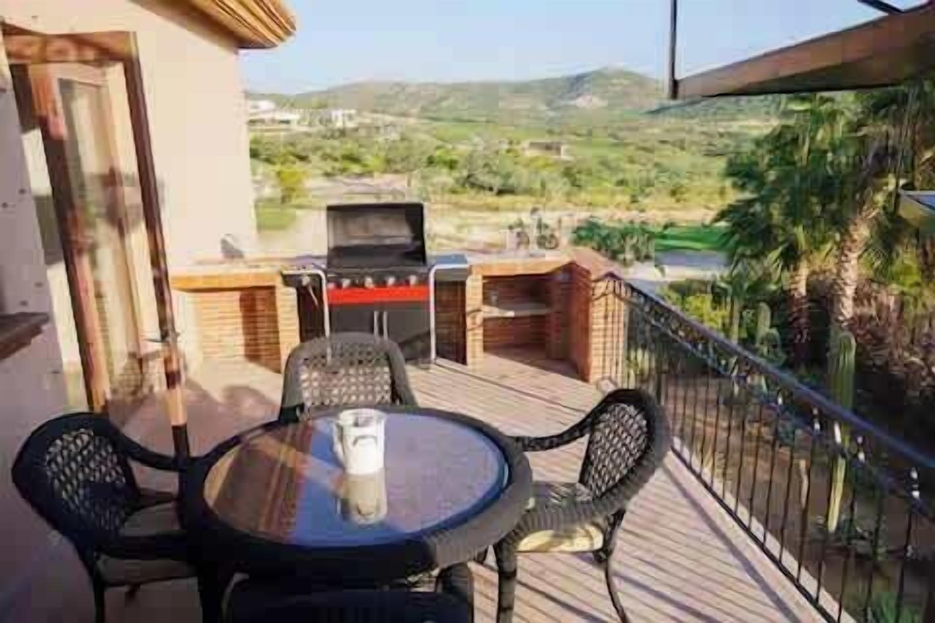 A balcony with a table, chairs, and a grill.