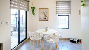 Un coin repas avec une table ronde et des chaises blanches, une plante suspendue, une œuvre d’art encadrée et un panier pour animal de compagnie.