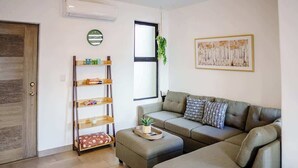 Un salon comprenant un canapé, un pouf et une étagère en bois.