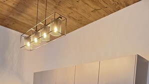 Une cuisine moderne avec des meubles blancs, une cuisinière noire, un évier et un plafond en bois.