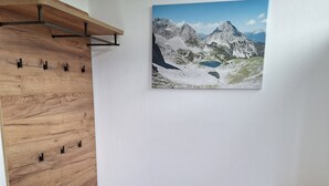 Une pièce avec un étagère en bois fixée au mur, un petit banc en bois et un tableau représentant un paysage de montagne.