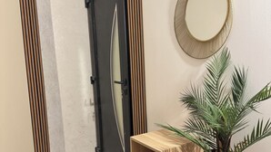 Un pasillo moderno con una puerta de madera, un espejo redondo, una consola de madera con una planta y un jarrón pequeño.
