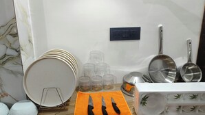 Un coin cuisine avec des murs en marbre blanc, une prise électrique noire et un plan de travail blanc sur lequel sont empilées des assiettes, des tasses et un bloc à couteaux.
