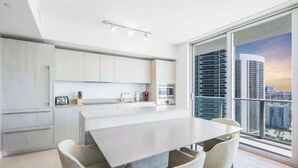 Une cuisine moderne dotée d’un grand îlot central, de meubles blancs et offrant une vue sur le paysage urbain grâce à de grandes fenêtres.
