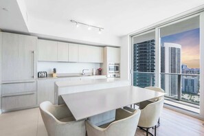 A modern kitchen with a large island, white cabinetry, and a view of a cityscape through large windows. - Ventur Luxe Condo l Oceanview | LYFE Beach Resort (Hollywood)