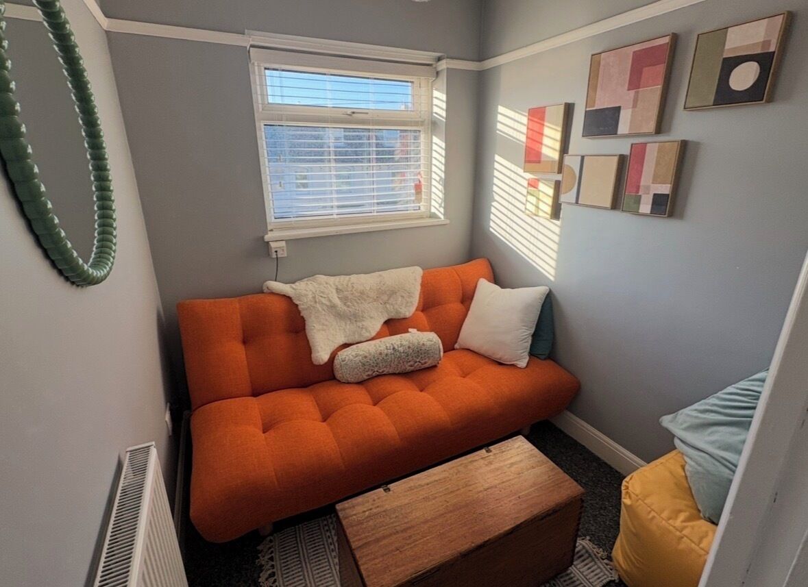 A cozy room with a tufted orange sofa, a wooden bench, and a window with blinds.