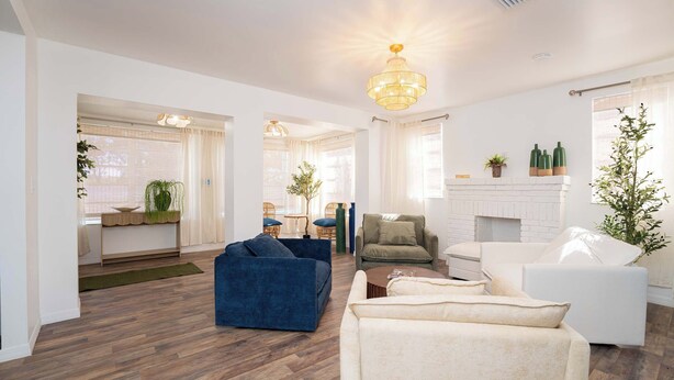 Un salón amplio con chimenea, un sillón azul, un sofá blanco y una zona de comedor con mobiliario de mimbre.