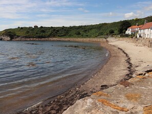 A coastal beach with a rocky shoreline, a sandy path, and buildings in the background. - Hay Loft (Anstruther)