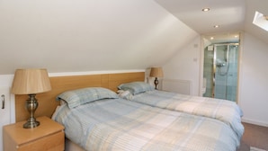 A bedroom with two beds, a nightstand, a lamp, and a shower area. - Hay Loft (Anstruther)