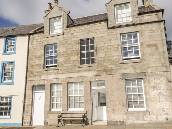 A stone building with multiple windows and doors, a bench outside, and a clear sky. - Maimies Harbourview (Anstruther)