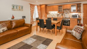 A cozy living room with a brown leather sofa, a dining area with a wooden table and chairs, and a kitchen with wooden cabinets and modern appliances. - Flour Loft (Anstruther)