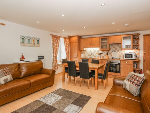 A cozy living room with a brown leather sofa, a dining area with a wooden table and chairs, and a kitchen with wooden cabinets and modern appliances. - Flour Loft (Anstruther)