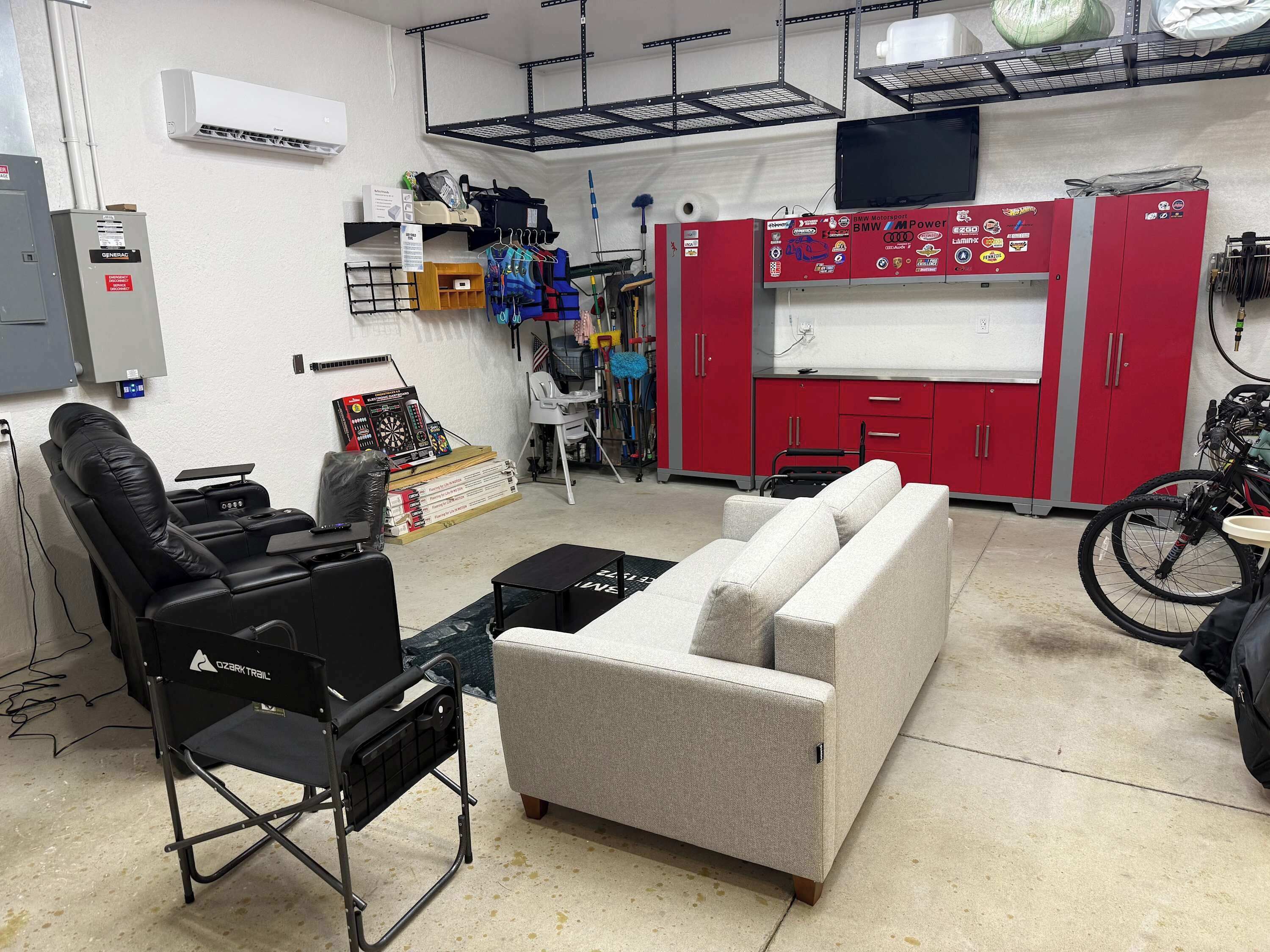 A room with a couch, a gaming chair, a small table, and a red cabinet with various items.