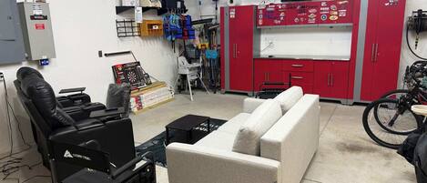 A room with a couch, a gaming chair, a small table, and a red cabinet with various items.