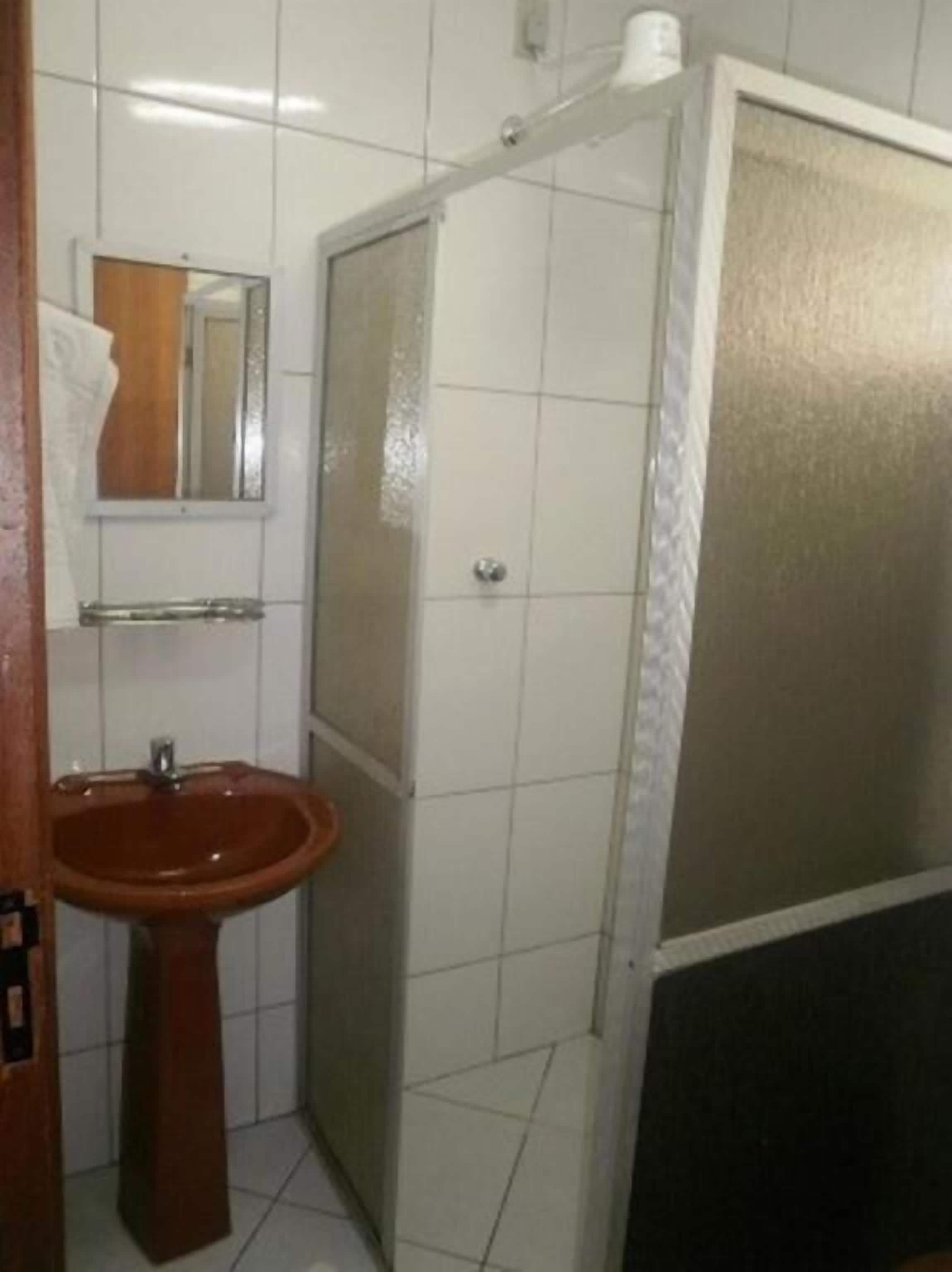 Un baño con lavamanos pedestal, espejo, cabina de ducha e inodoro.