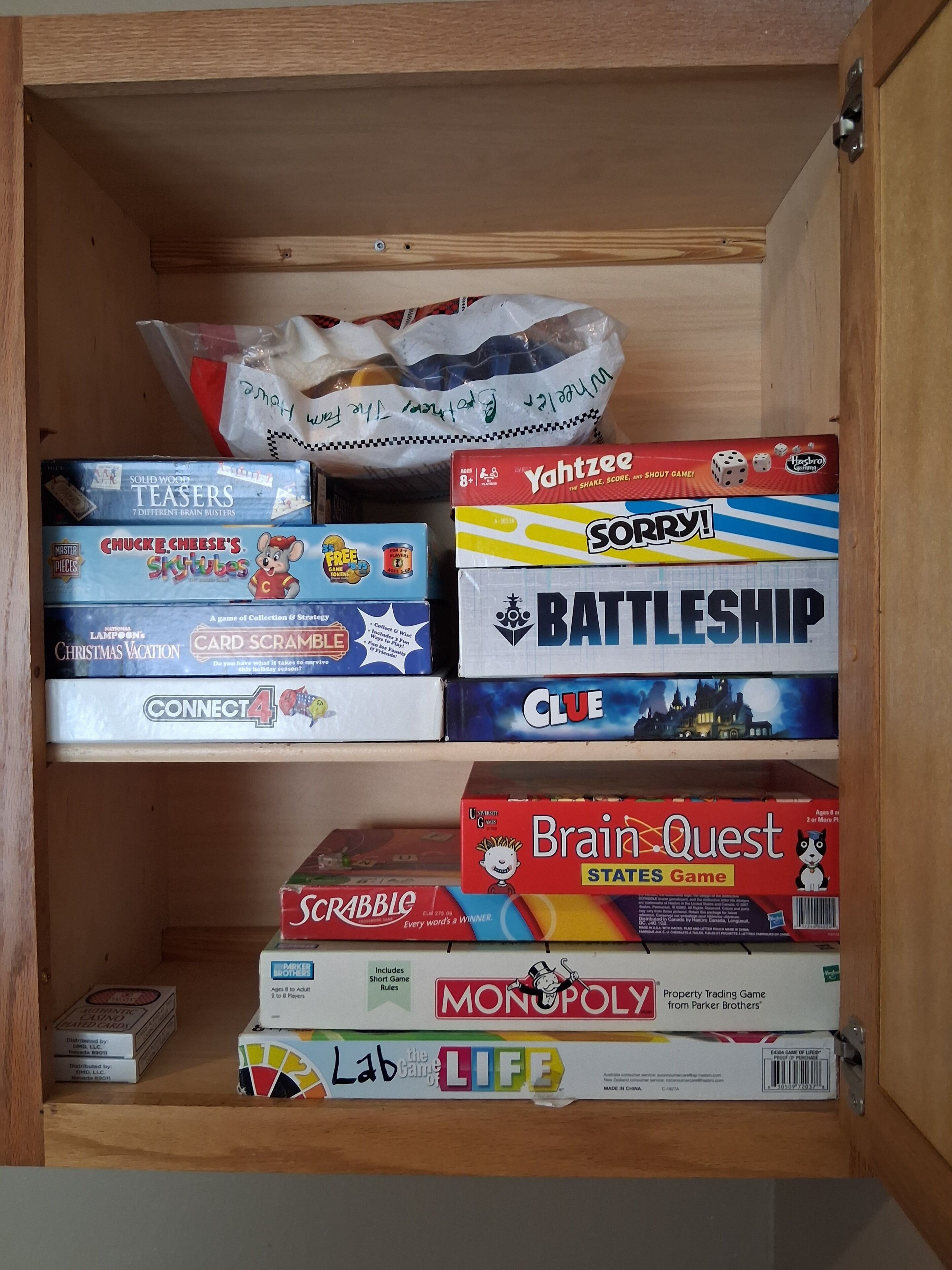 A wooden cabinet with various board games organized on shelves.
